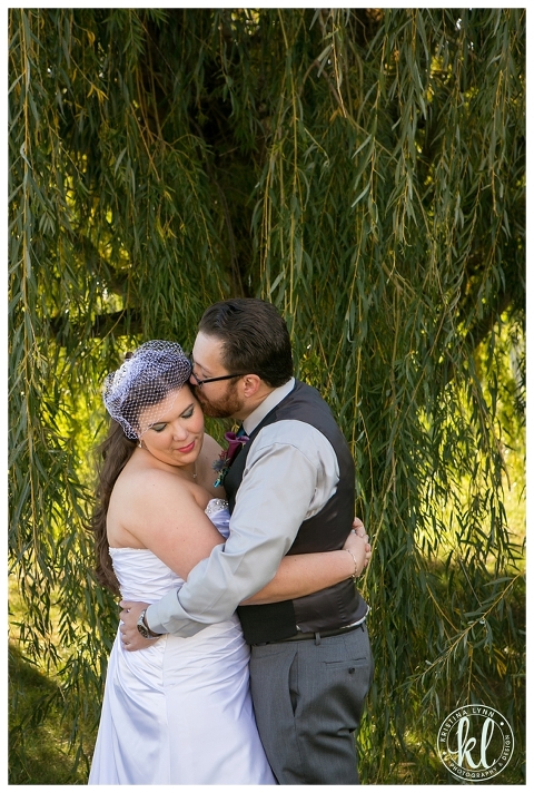 A wedding couple photographed under a giant willow tree on their farm in Iowa.