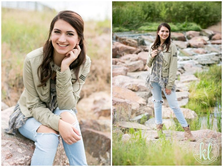 Teenage girl wearing a green jacket and light washed jeans on a rocky river bed.