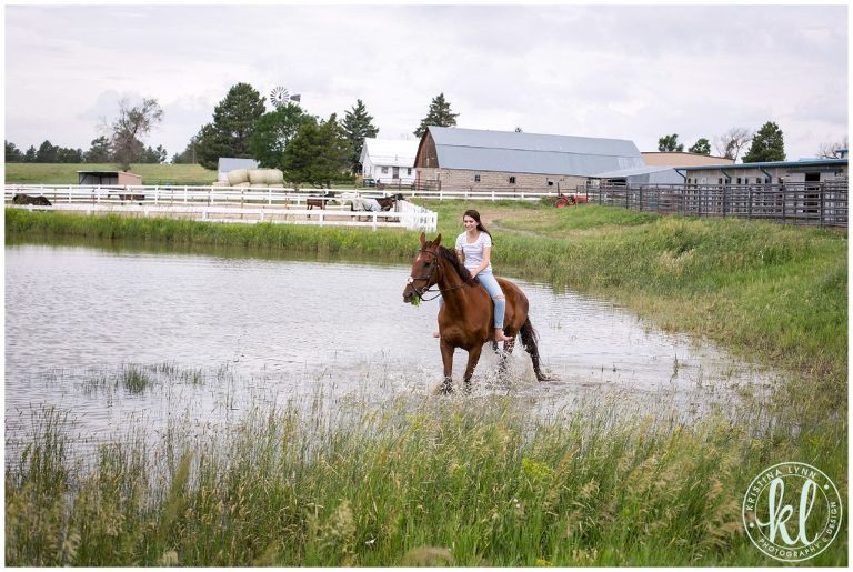 A young girl riding her horse through a water hole on a farm in rural Minnesota