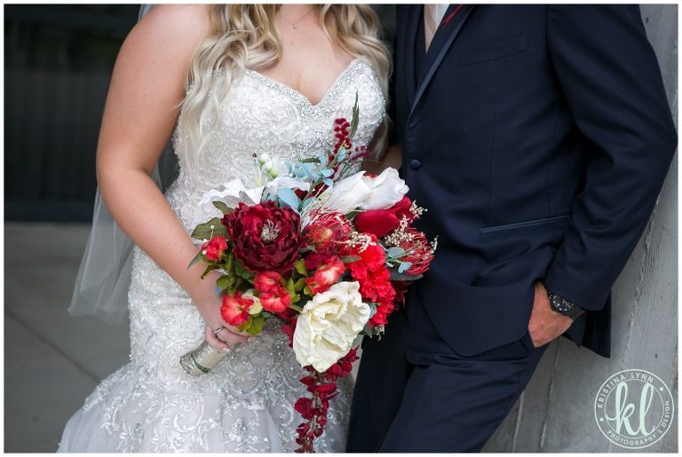 Closeup detail of the bride's bouquet made of of red and white florals with a pop of slate blue.
