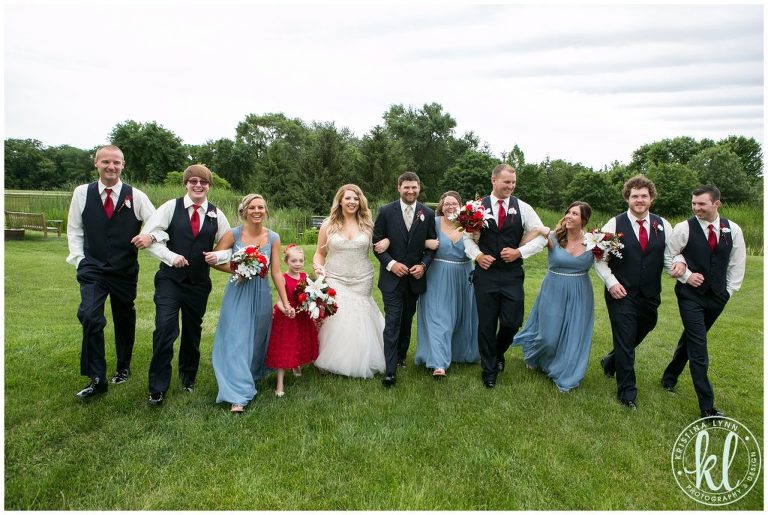 Wedding party linking arms and walking through grass at Reiman Gardens in Ames Iowa