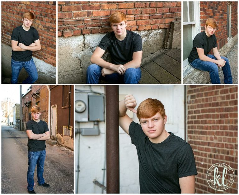 teenage guy posing for senior pictures against red brick wall in alleyway