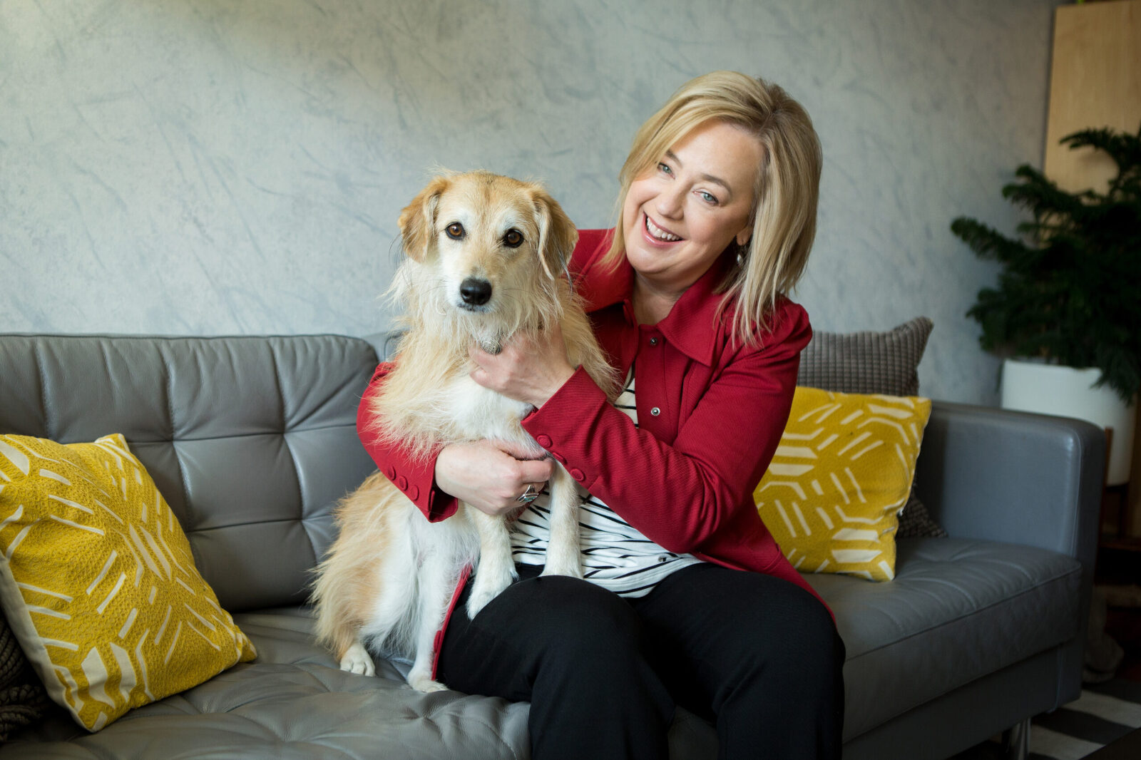 An in home photo shoot of a woman and her dog. She holds the dog to her with an arm around it. She is petting the dog and smiling.