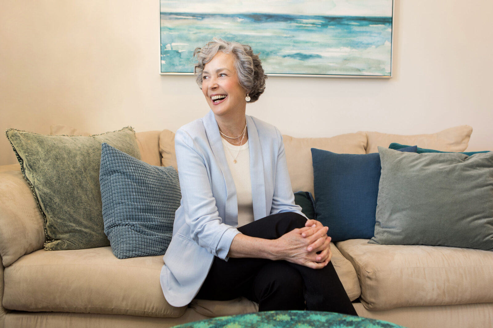 business professional woman seated on couch with her legs crossed, looking off to the side and smiling brightly