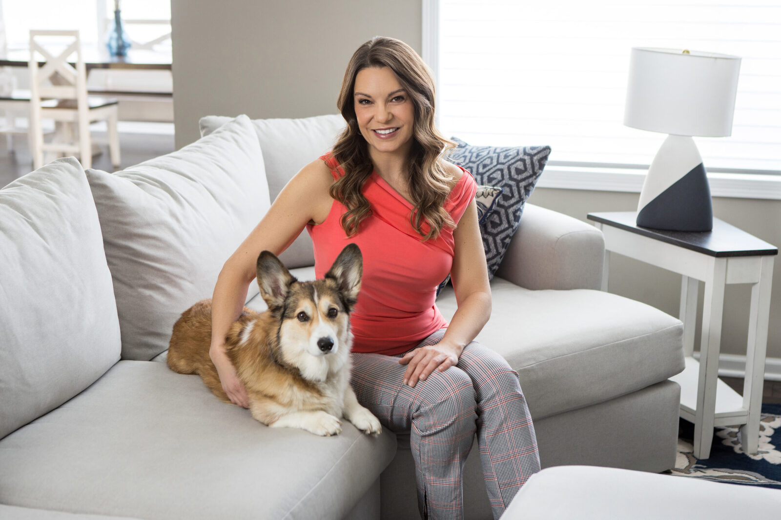 An in-home lifestyle session with a woman and a corgi on a grey couch.