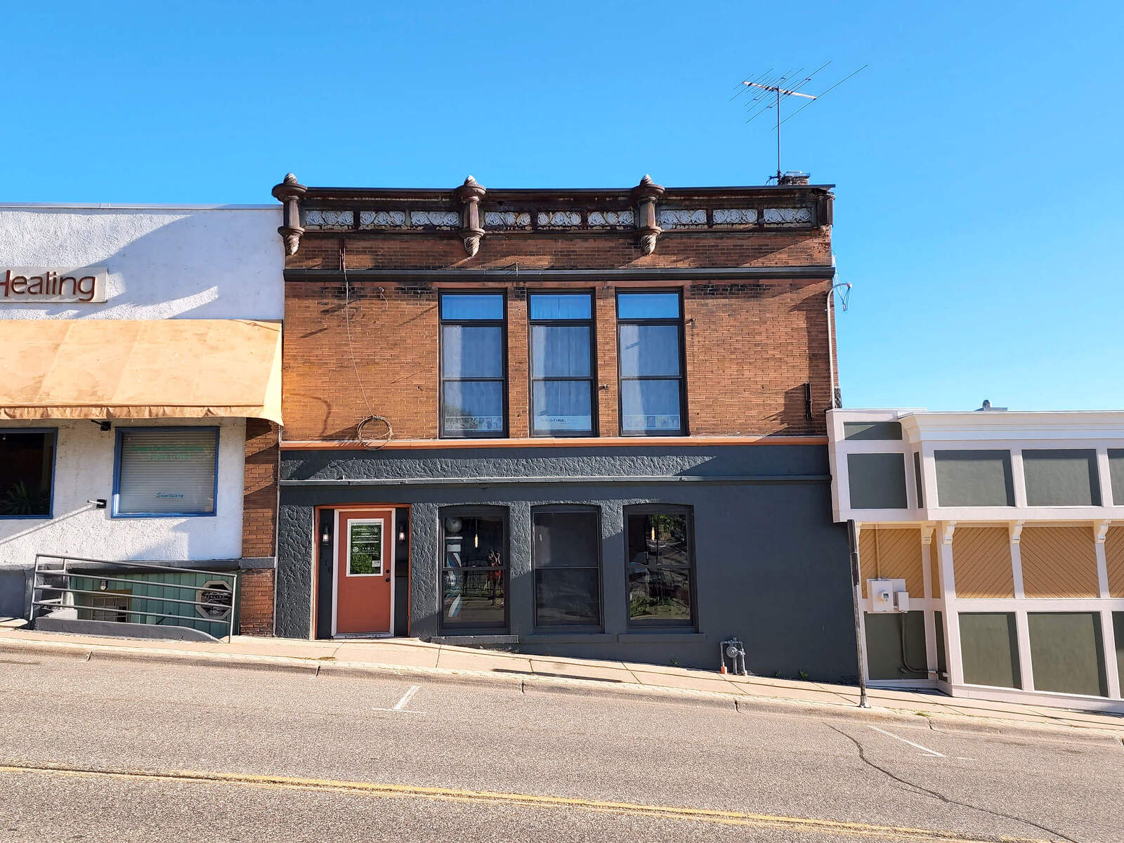 The photo is taken from the middle of a street facing a brick building. The brick is orange/red on top and black on bottom. There is no signage on the building.