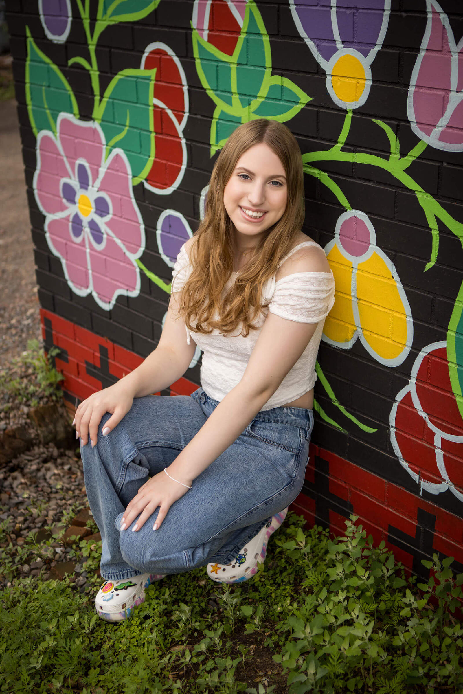 A high school senior girl poses in front of an art mural for her senior photos.